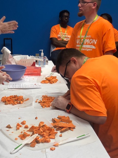 A young man in an orange shirt is carefully cutting sweet potatoes