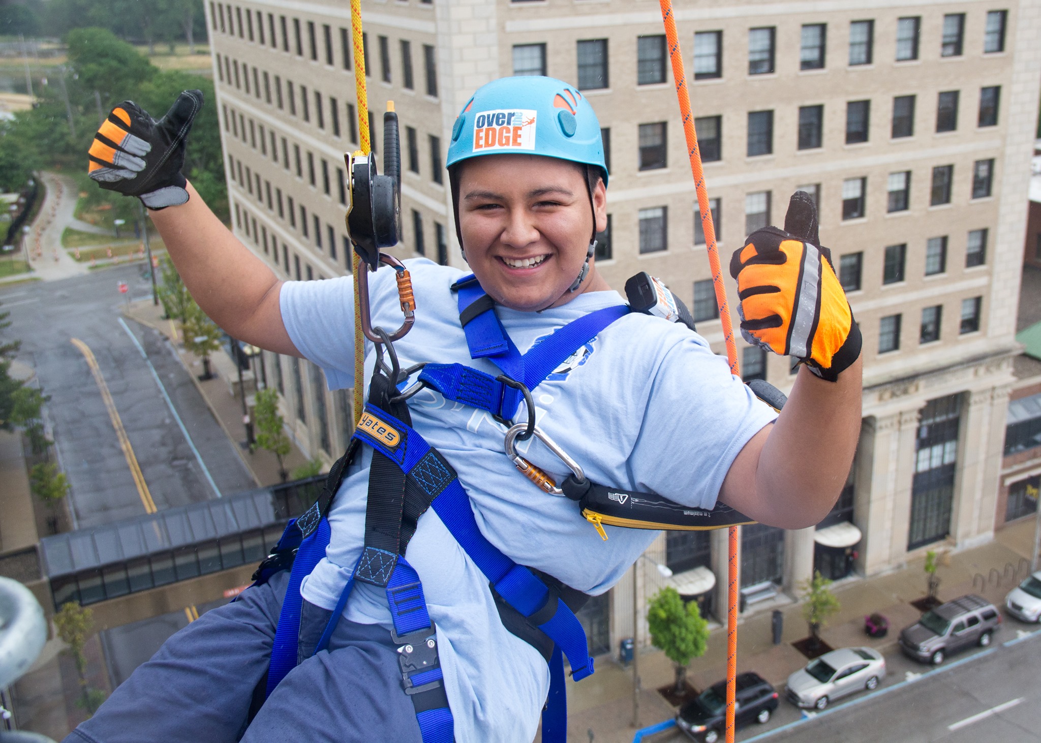 A young person grins, holding two thumbs up at the camera before they go Over the Edge.